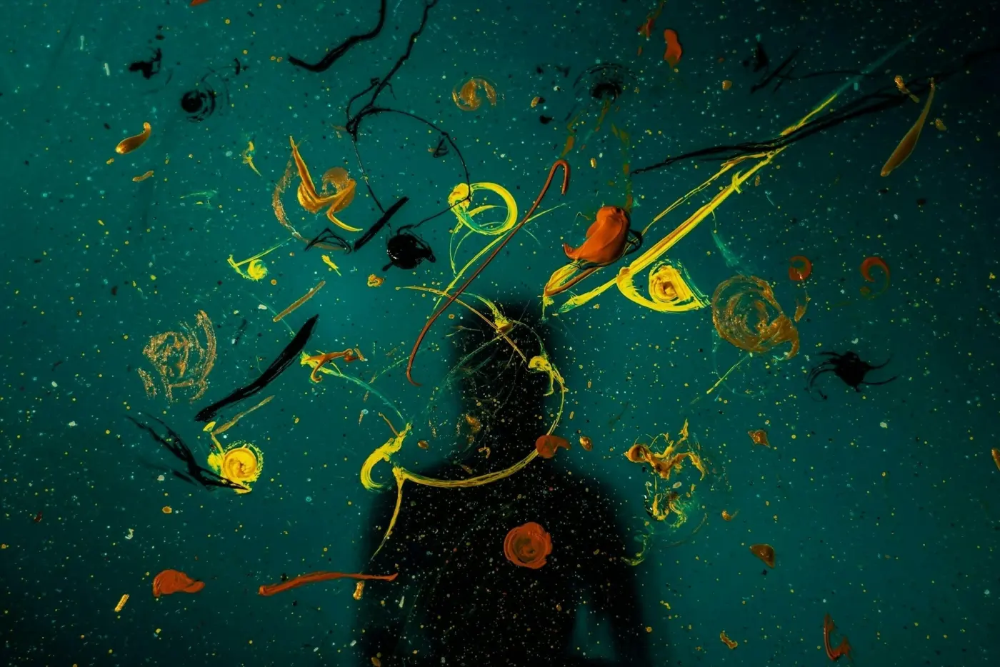 Auto-generated description: A silhouette is visible against a dark backdrop with splatters of bright orange and yellow paint creating an abstract design.