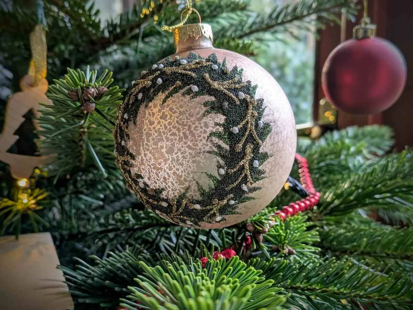 Close-up of silver bauble featuring a wreath design, hung on a Christmas tree