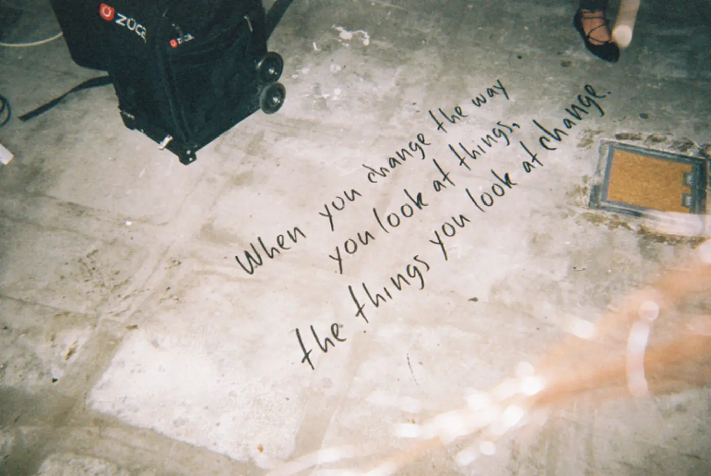 Concrete floor with handwritten quote and a black case in the corner.
"When you change the way you look at things, the things you look at change."