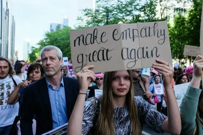 A young woman holding a sign reading 'Make empathy great again'