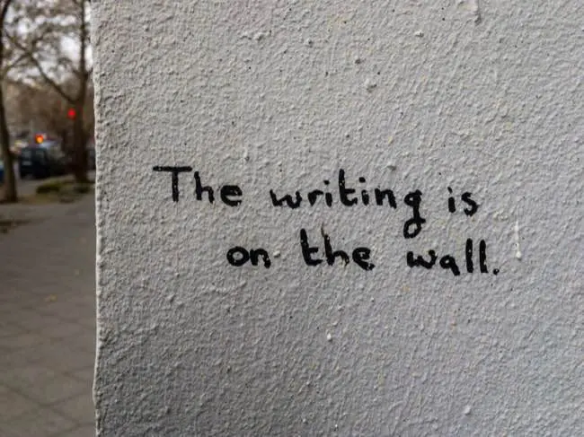 Auto-generated description: A wall contains the handwritten message The writing is on the wall.
