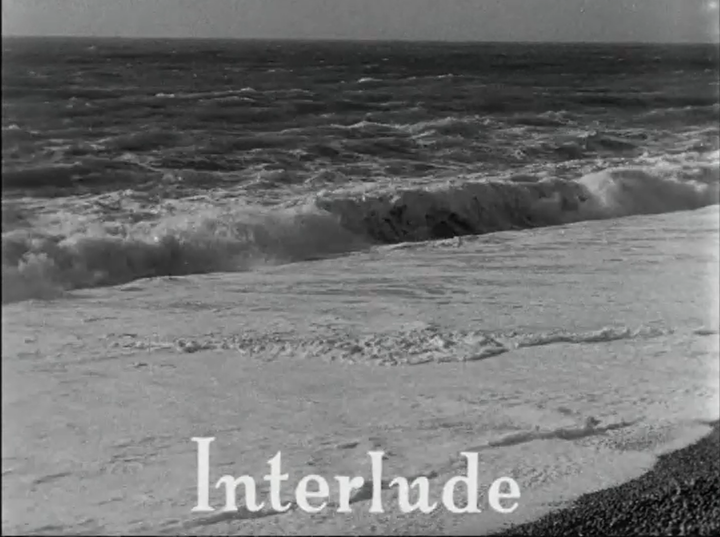 Auto-generated description: Waves crash onto a pebbled beach, accompanied by the text Interlude.